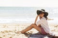 Summer vacation concept. Happy young woman relaxing on beach. Hipster slim girl in white shirt and hat sitting and tanning on Royalty Free Stock Photo