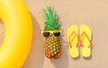 Summer vacation concept - pineapple and inflatable ring with yellow flip flops on beach on sand background Royalty Free Stock Photo