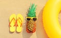 Summer vacation concept - pineapple and inflatable ring with yellow flip flops on the beach on sand background Royalty Free Stock Photo