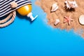 Summer vacation concept with seashells, starfish, women`s beach bag and suntan lotion bottle on a blue background and sand