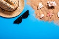 Summer vacation concept with seashells, starfish, women`s beach hat and sunglasses on a blue background and sand. Royalty Free Stock Photo