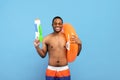 Summer vacation. Handsome black man with inflatable ring and water gun smiling at camera over blue studio background Royalty Free Stock Photo