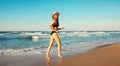 Summer vacation, happy smiling woman walking running in bikini swimsuit and straw hat on the beach on sea coast with waves Royalty Free Stock Photo