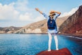 Summer vacation. Happy traveler woman feels free raising arms on rock on Red beach on Santorini island, Greece Royalty Free Stock Photo