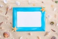 Blue wooden frame with white paper sheet, seashells and starfish on sand background. Royalty Free Stock Photo