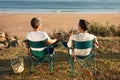 Older couple sitting together facing ocean enjoying coffee at seaside