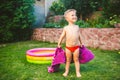 Summer vacation theme. A small 3 year old Caucasian boy playing in the backyard of a house on the grass near a round inflatable co