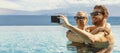 Summer vacation - young happy couple taking selfie with phone in resort swimming pool. copy space Royalty Free Stock Photo