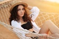 Summer vacations concept, Happy woman with black bikini, hat and white shirt relaxing in hammock on tropical beach at sunset Royalty Free Stock Photo