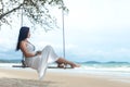 Summer Vacations. Lifestyle women relaxing and enjoying swing on the sand beach, fashion stunning women with white dress on the tr Royalty Free Stock Photo