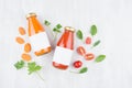 Summer vegetable juices of tomato and carrot in glass bottles with blank label, ingredients and green leaves on white wood board.