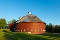 Summer view of early 20th century wooden circular red barn with gambrel roof