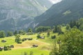 Summer view of green grassy alpine meadows with some houses and wooden barns. Big swiss mountains in the background. Royalty Free Stock Photo