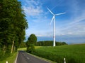 Summer view on white wind generator and empty car road among green fields and green trees with blue sky and white clouds backgroun Royalty Free Stock Photo