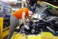 An employee of an automobile plant assembles an engine under the hood of a new car
