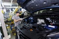 An employee of an automobile plant assembles an engine under the hood of a new car