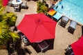 Summer weekend at the country club with bright red sunbrellas and palm trees and turquoise swimming pool surrounded by lounge Royalty Free Stock Photo