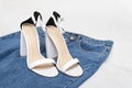 Summer white sandals with comfortable high heels and blue jeans on white background. Everyday casual outfit