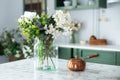 Summer white wild flowers in vase and turk with coffee in kitchen table. Bouquet of flowers and plants in glass vase at home.