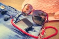 Summer women's accessories: red sunglasses, beads, denim shorts, mobile phone, headphones, a sun hat. Toned image