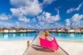 blond girl walking on the beach with a pink beach scarf. Luxury beach villas and wooden pier pathway Royalty Free Stock Photo