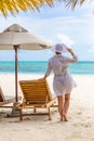 Young woman relaxing at tropical beach during summer vacation, white dress hat, beach shore, umbrella and chairs