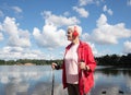 Outdoor shot of healthy energetic elderly female walking on the beach sunny day using Nordic poles.