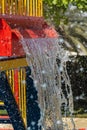 Summertime fun for the kids at the splash pad to play with water falling from bright colored red fountain to pool below portrait Royalty Free Stock Photo