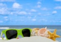 Summertime image of starfish, shells and bright green sunglasses piled on sand. Ocean in the background. Royalty Free Stock Photo
