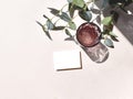 Summertime minimal mockup still life scene with blank invitation card, color glass and eucalyptus branch on beige background.