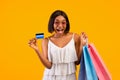 Summertime sales. Excited black woman with shopping bags showing credit card, shouting OMG on orange background Royalty Free Stock Photo