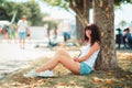 Summertime. A smiling woman is sitting relaxed leaning against a tree trunk. Recreation in the Park Royalty Free Stock Photo