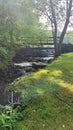 Summertime step waterfall under walking bridge with trees and grass at New England park