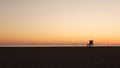 Summertime travel concept. Dark silhouette, iconic retro wooden lifeguard watch tower against sunset orange sky. Contrast