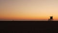 Summertime travel concept. Dark silhouette, iconic retro wooden lifeguard watch tower against sunset orange sky. Contrast