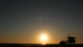 Summertime travel concept. Dark silhouette, iconic retro wooden lifeguard watch tower against sunset orange sky. Contrast