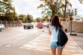 Summertime. Woman with a tattoo on her arm with backpack, standing at a pedestrian crossing. Rear view. Concept of traffic and Royalty Free Stock Photo