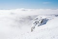 The summit of a snowy mountain with a clear blue sky on a sunny day overlooking the valley covered by fog Royalty Free Stock Photo