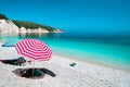 Sun beach umbrellas on a pebble beach with azure blue calm sea, white rocks and clear sky in background Royalty Free Stock Photo