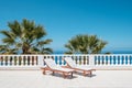 Two sun beds on villa terrace with ocean and palm tree background