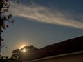 The sun begins to hide behind the roof of a house