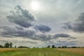 The sun behind gray clouds in the sky, the horizon and field stripes Royalty Free Stock Photo