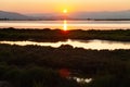 Sun setting behind mountains and reflecting in ebro river and sea in ebro delta national park in catalunya, spain, with warm Royalty Free Stock Photo