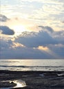 Sun with Bright, Golden Yellow and Orange Aura, behind Dark Clouds and Sunlight falling on Calm Sea Water through Clouds in Sky Royalty Free Stock Photo