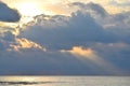 Sun with Bright, Golden Yellow and Orange Aura, behind Dark Clouds and Sunlight falling on Calm Sea Water through Clouds in Sky Royalty Free Stock Photo