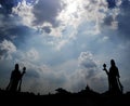 Sun casts rays from behind clouds and makes a strong silhouette of a pair of statues and the temple rooftops