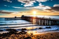 The sun casts warm glow on vibrant clouds above expansive ocean framing old pier against sandy beach Royalty Free Stock Photo