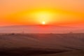 The sun caught during the last moment before setting beyond the horizon with view of a field covered with fog and the farms and