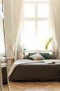 Sun coming through a large window and shinning onto a bed with earth color linen in a wooden floor bedroom interior. Part of the b