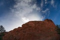 Sun coming up from behind a bare rock mountain, blue sky and clouds, Colorado American west